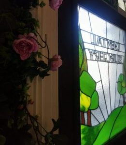 Stained glass window with green landscape and text, next to pink roses, in a dental practice reception area in Brighouse, Huddersfield, Halifax, and Bradford.