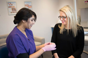 A woman in purple dental scrubs showing a dental model to a smiling female patient wearing glasses in a modern dental clinic.